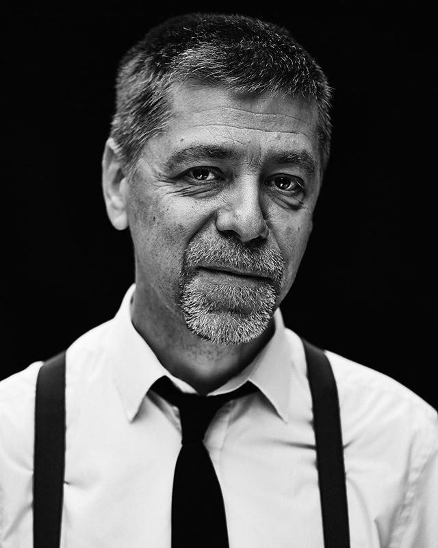 A black and white portrait of a man wearing a tie and suspenders, with a serious expression.