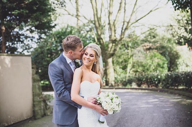 A bride and groom share an intimate moment at their outdoor wedding, surrounded by lush greenery.
