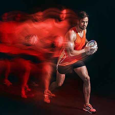 A dynamic shot of a male rugby player running with a ball, captured with motion blur for a sense of energy and intensity.