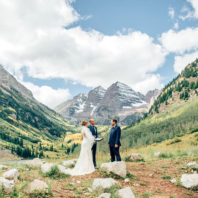 A bride and groom exchange vows during an outdoor wedding ceremony in a scenic mountain landscape.