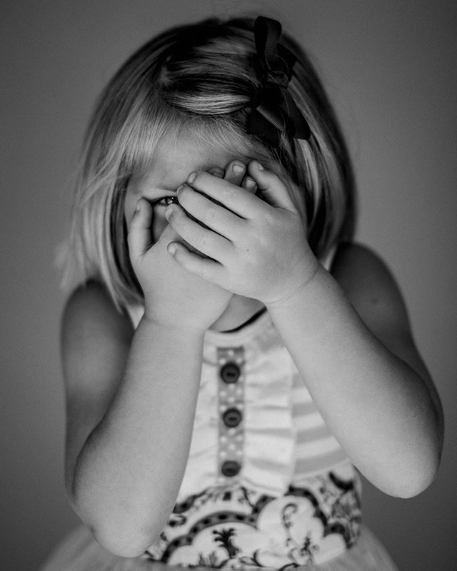 A young girl covers her face with her hands in a close-up black and white portrait.