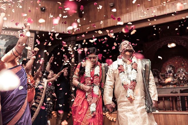 A bride and groom are showered with flower petals during their traditional Indian wedding ceremony with family.