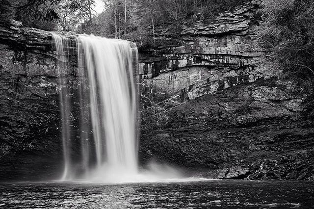 A black and white long exposure shot of a scenic waterfall surrounded by rocks and trees.