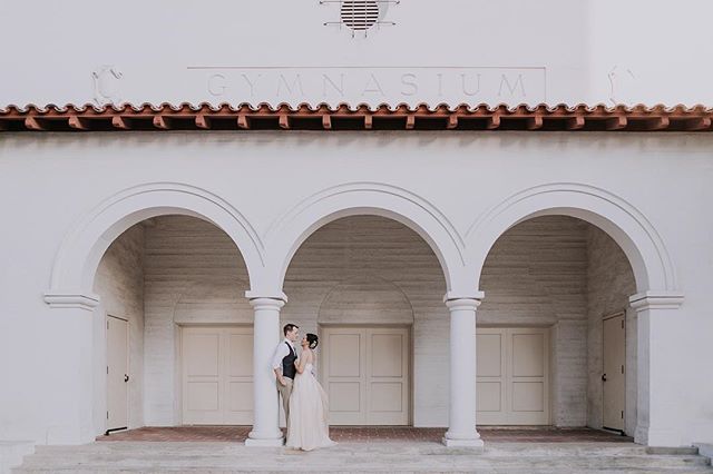 A bride and groom embrace in front of a building with arches for an elegant wedding photo.