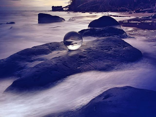 A tranquil beach scene featuring a lensball on rocks, capturing the serene beauty of the shoreline and blurred waves.