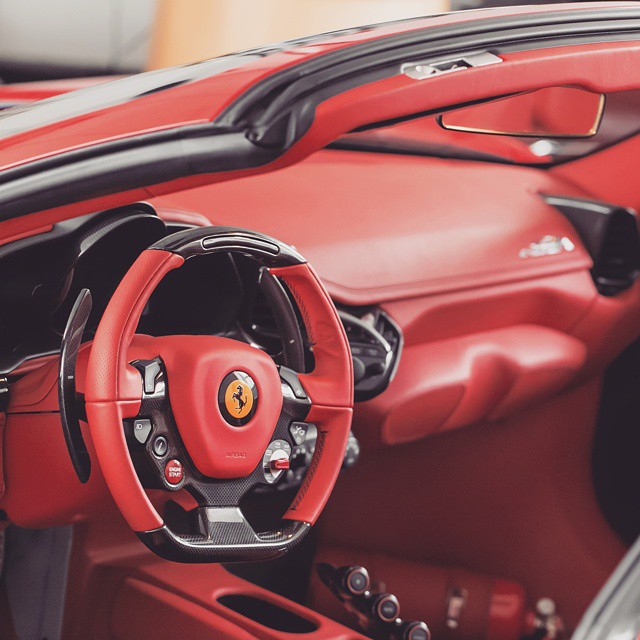 A close-up of the red interior and steering wheel of a sleek Ferrari sports car.