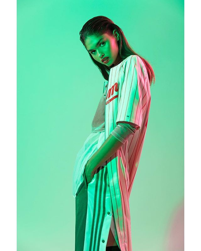 A woman poses in modern sportswear with a baseball jersey in a studio setting.