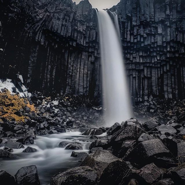 Majestic waterfall cascading down basalt columns in Iceland, surrounded by rocks and serene nature.