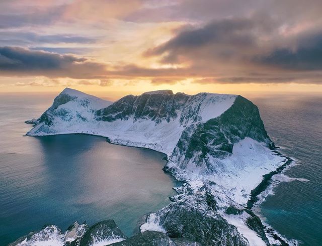 A serene aerial view showcases snow-capped mountains meeting the ocean in a tranquil Norwegian landscape.