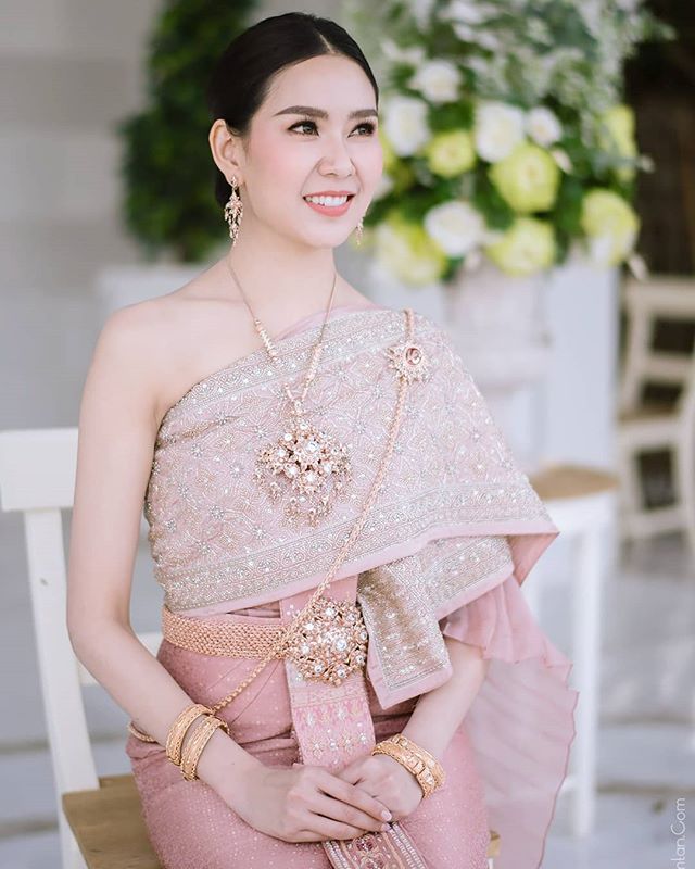 A woman smiles in traditional Thai dress, adorned with jewelry, for a wedding or formal event.