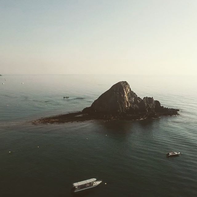 Scenic aerial view of an island with a rocky peak surrounded by ocean and boats.
