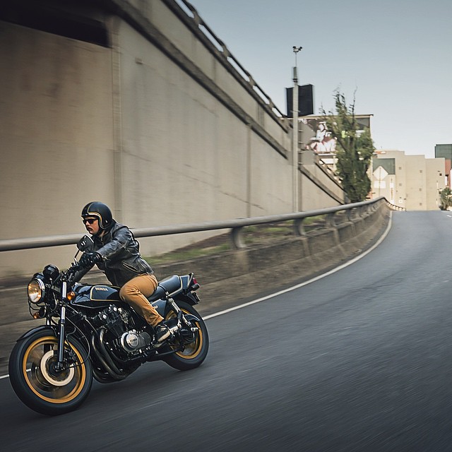 A motorcyclist rides a vintage Honda motorcycle on a city street.