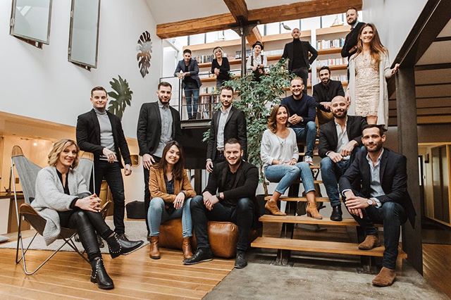 A team of professionals poses together in a modern office setting with stairs and a cheerful atmosphere.