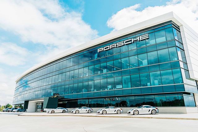 Exterior view of a modern Porsche office building with luxury cars parked in front, showcasing corporate success and automotive excellence.