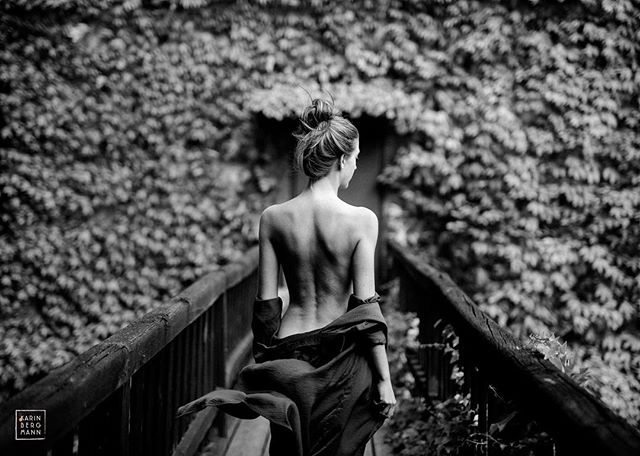 A woman walks across a bridge surrounded by lush greenery in this black and white image.