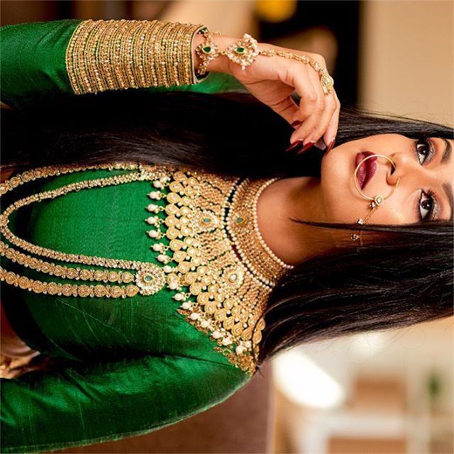 Woman adorned in traditional Indian jewelry and a green dress, showcasing elegance and culture.