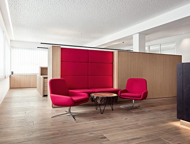 Modern office seating area with red chairs, wood table, and neutral tones creates a welcoming and professional environment.