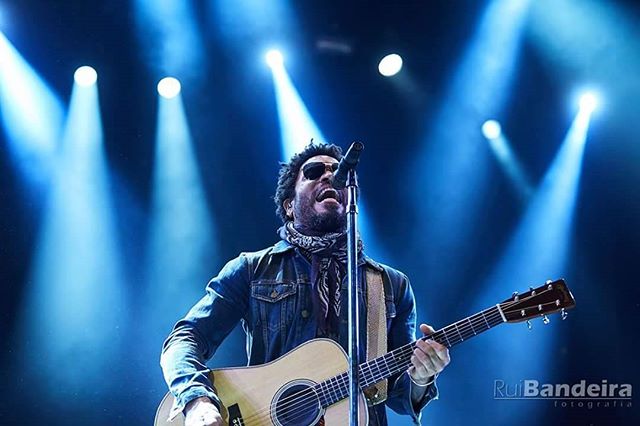 A musician passionately sings and plays guitar on a brightly lit stage during a live concert.