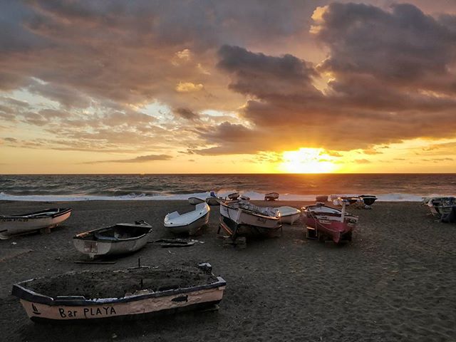 Boats rest on a sandy beach during a tranquil sunset over the ocean, a peaceful coastal scene.