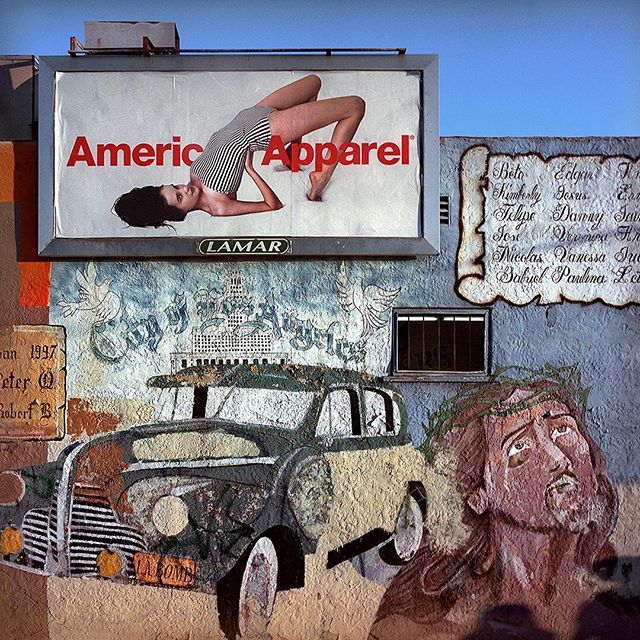 A gritty urban mural featuring a vintage car, Jesus, and an American Apparel ad, capturing street art's raw essence.