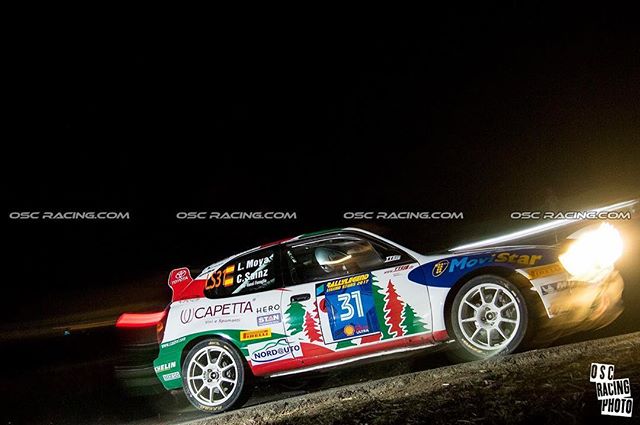 A rally car speeds through the night in a motorsport event, showcasing action and energy.