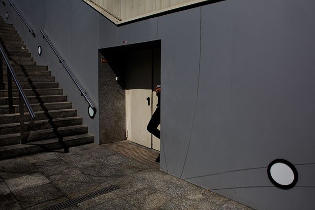 A person emerges from a doorway at the bottom of a gray urban stairwell.