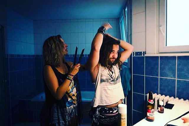 A woman styles a man's hair in a bathroom with beauty products and a beer on the counter.