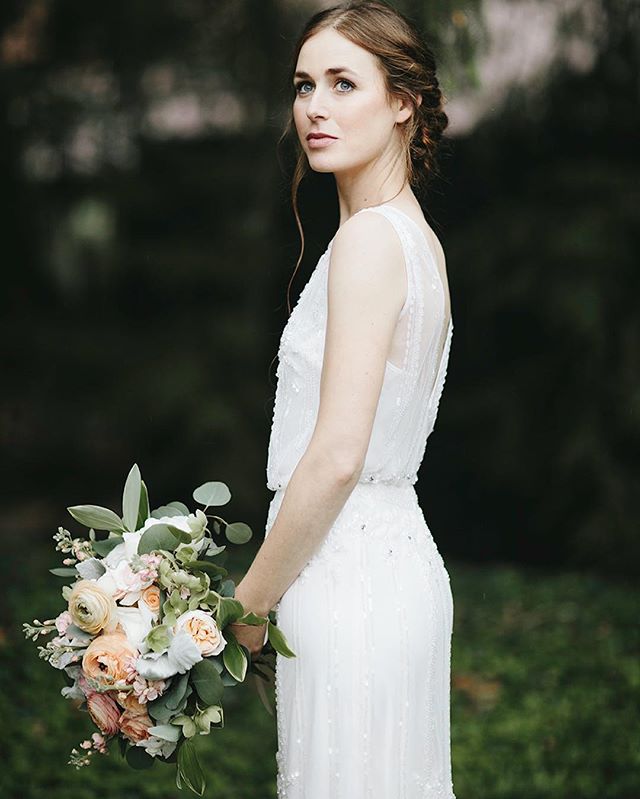 A bride in a white dress holds a bouquet of peach and white flowers, looking off to the side.