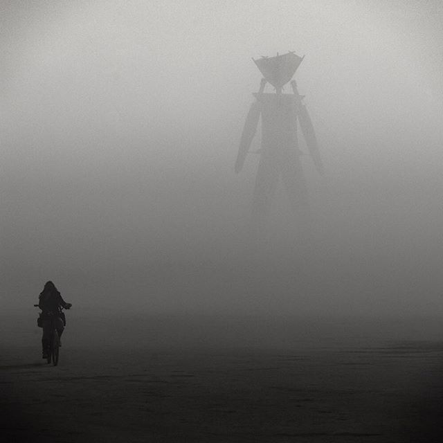 A person rides a bike through the fog toward a large structure at Burning Man.