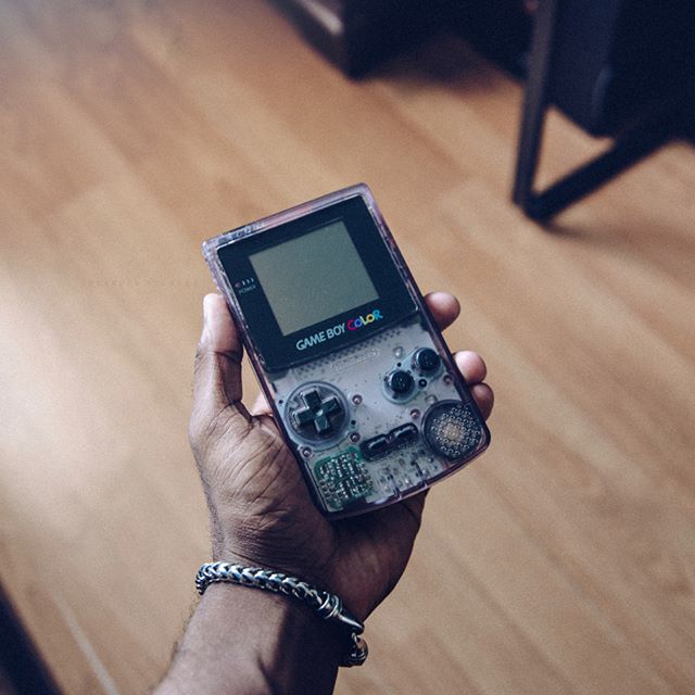 A clear purple game boy color handheld console being held over a wooden floor.
