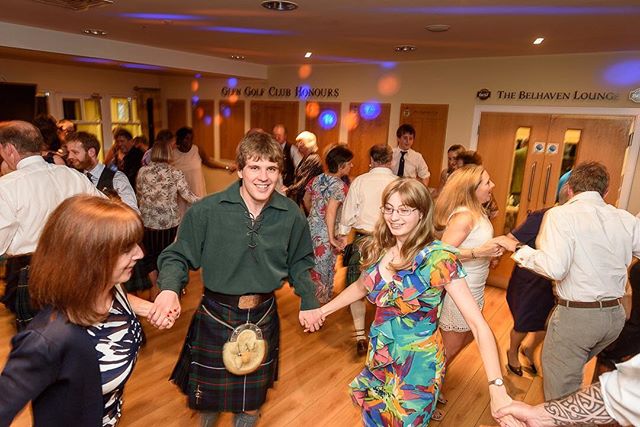 People enjoy Scottish dancing at an indoor event, with traditional kilts and cheerful atmosphere.