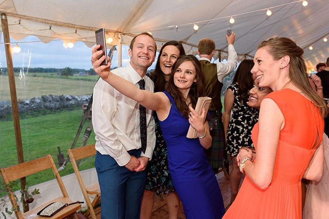 A group of friends gather for a selfie at a wedding celebration inside a tent.