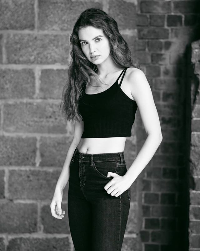A young woman poses in black and white against a brick wall, conveying confidence and urban style.