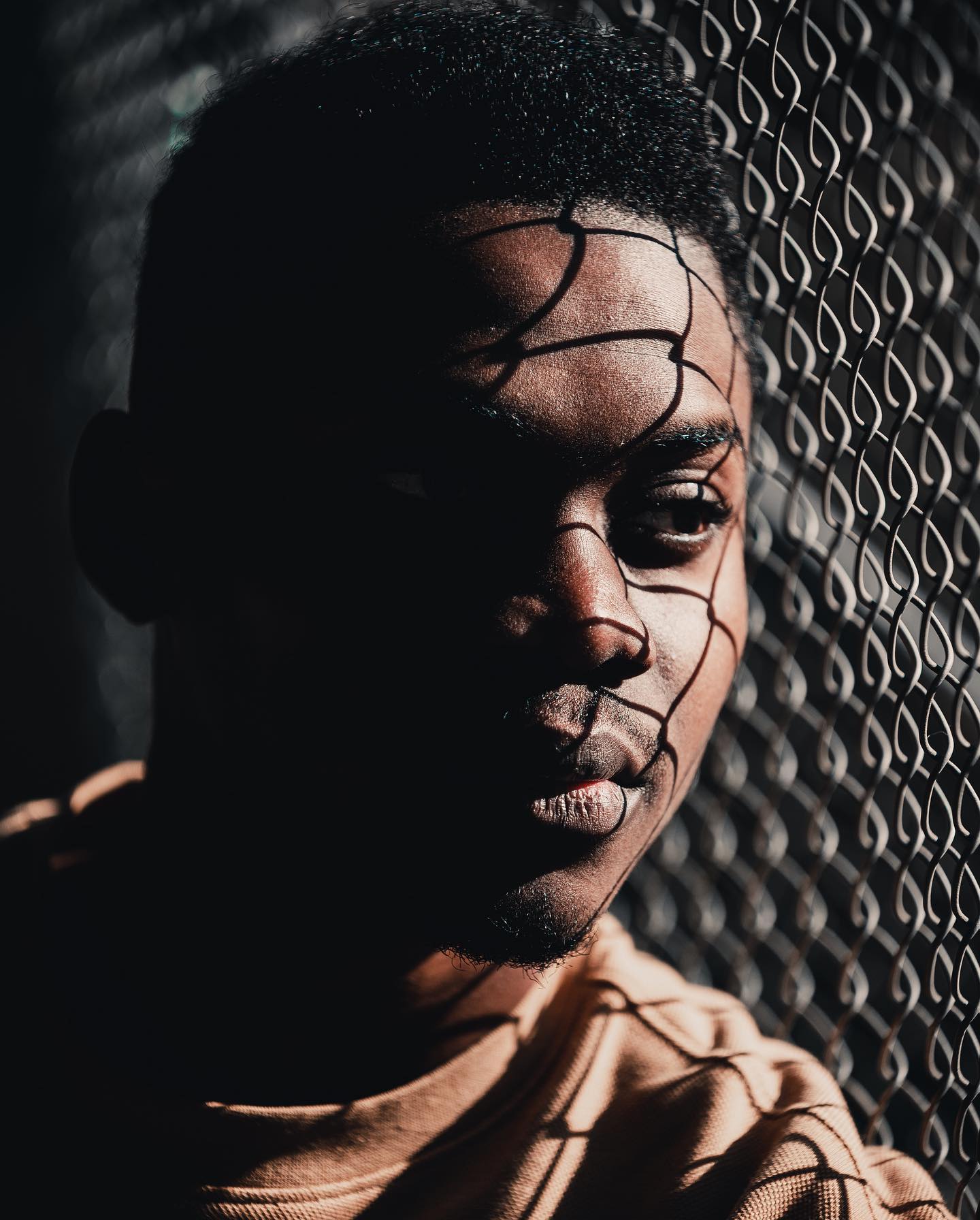 A striking portrait of a man behind a metal grid, creating a dramatic shadow pattern on his face.