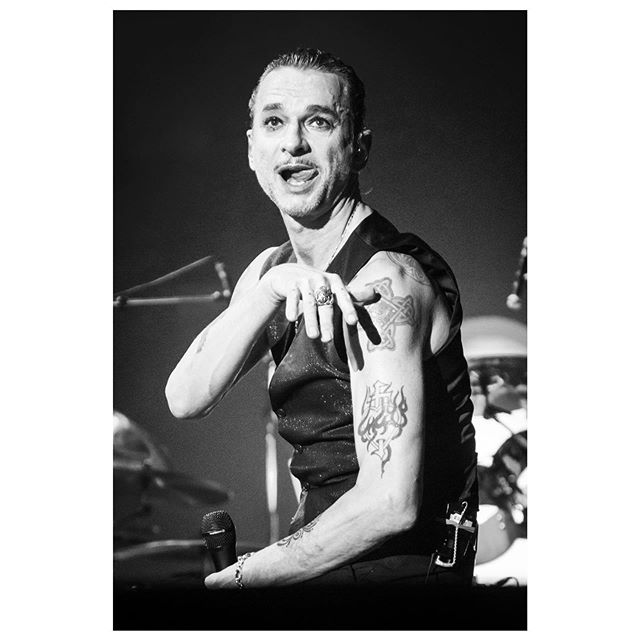 A black and white medium shot of singer David Gahan performing on stage with a microphone.