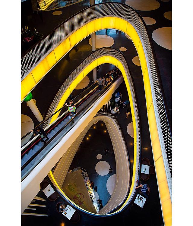 High angle view of people on an escalator in a shopping mall, with tables and chairs.