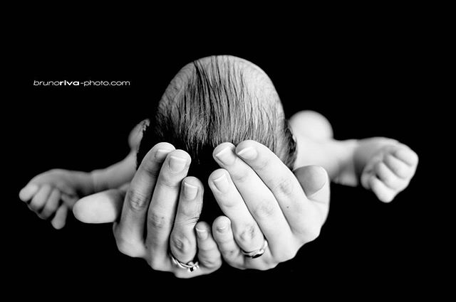 A parent's hands gently cradle a newborn baby in a loving and protective embrace, set against a dark background.