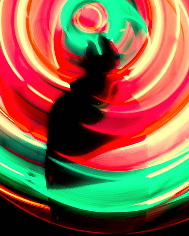 A silhouetted figure stands against an abstract swirl of red, green, and yellow light trails created using long exposure photography.