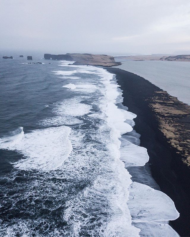 A dramatic black sand beach meets the ocean under an overcast sky in Iceland, creating a serene and scenic landscape.