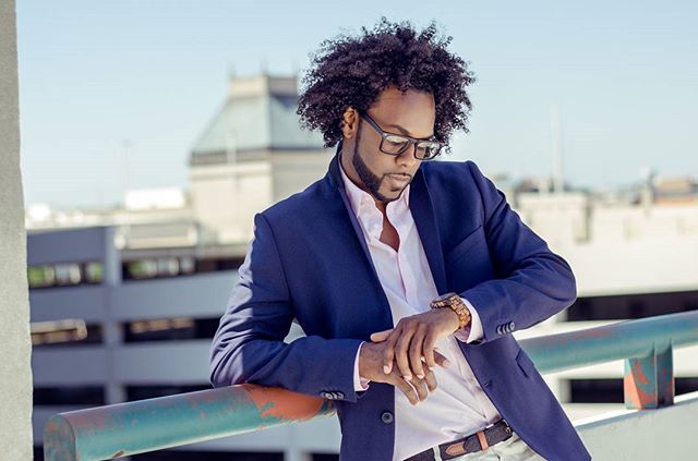 A stylish man with glasses checks his watch against an urban backdrop, exuding confidence and professionalism.