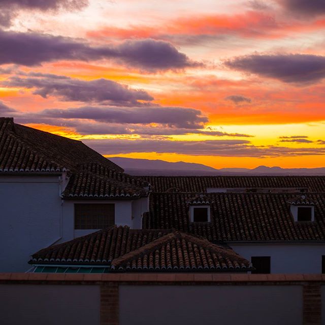 Warm sunset colors paint the sky over rooftops and mountains in this tranquil cityscape.