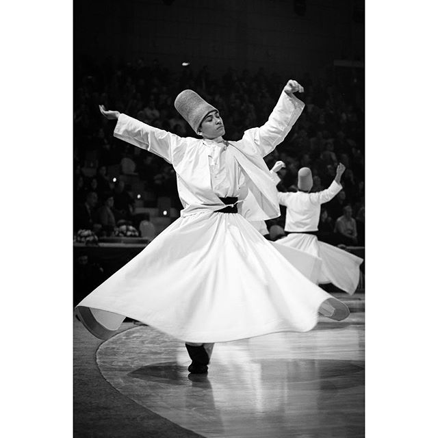 A black and white photo of whirling dervishes performing a traditional dance in a performance hall.