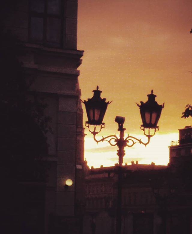 Vintage street lamps silhouette against a warm sunset in a historic city, creating a dreamy and tranquil urban scene.