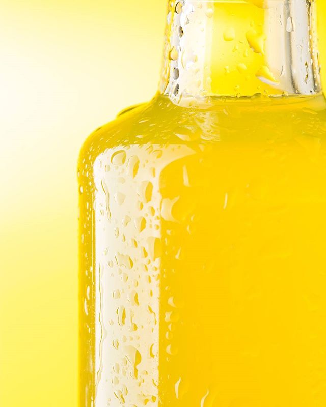 A vibrant yellow drink in a glass bottle with water droplets on a bright yellow background.