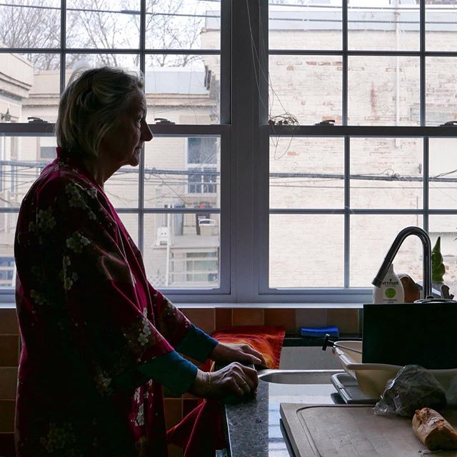 A woman stands in her kitchen, looking out the window next to the sink and countertop.