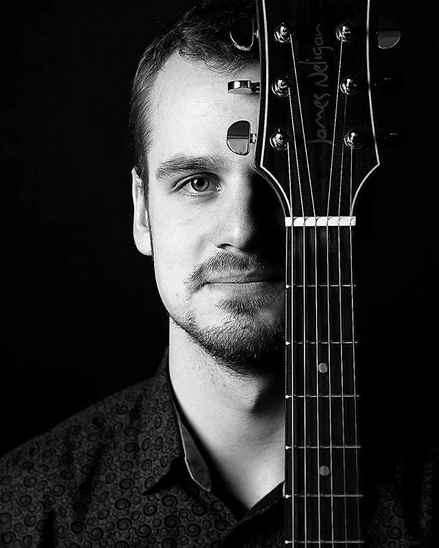 A black and white close-up of a man with a guitar covering half his face.