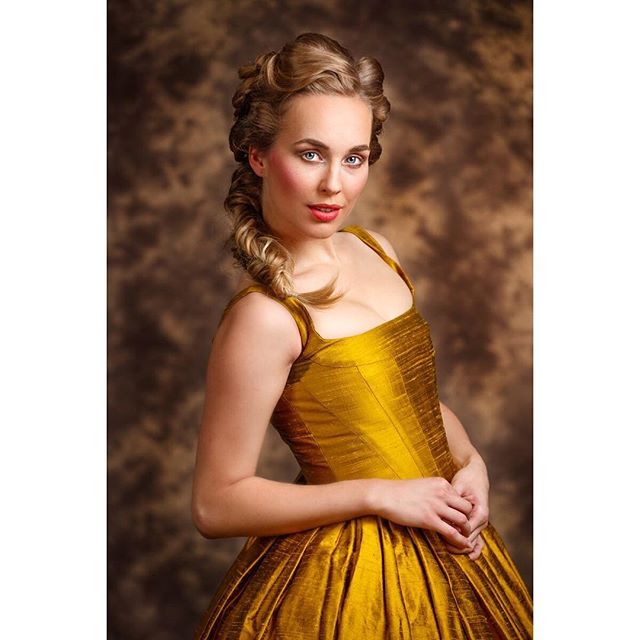 Elegant woman with blonde hair wearing a gold dress in a vintage style, posing for a portrait in a studio.
