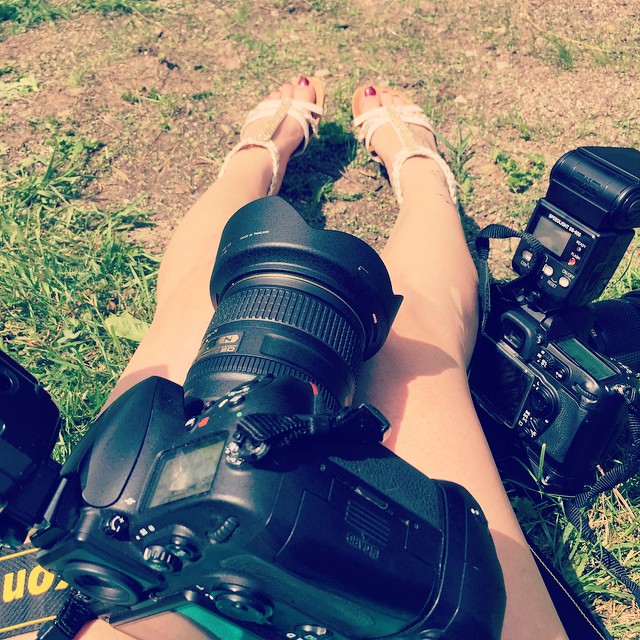 A relaxed photographer rests on the grass with camera equipment and sandals.