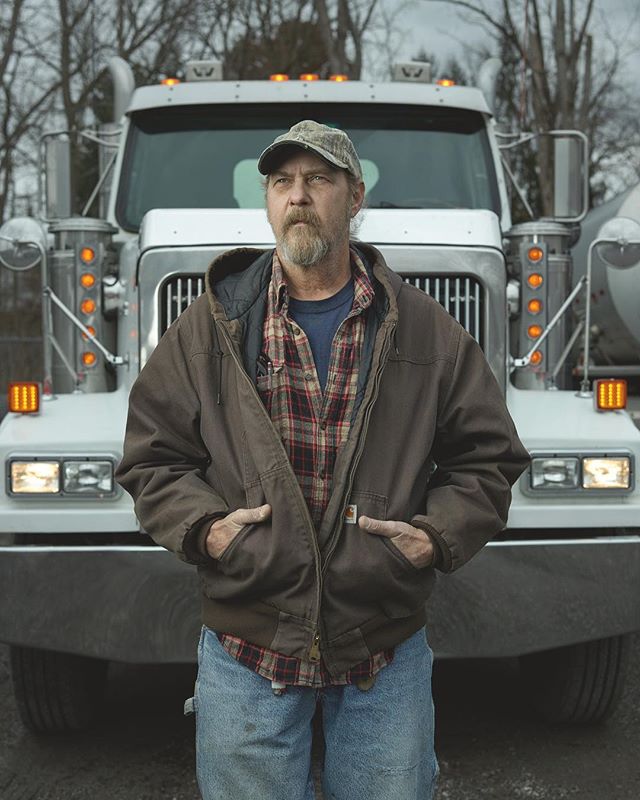 A truck driver stands in front of his truck with his hands in his pockets.