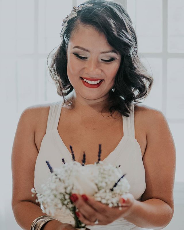 A smiling woman in a white dress holds a flower bouquet, captured with soft lighting.